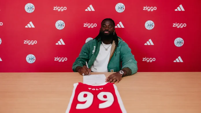 Tolu Arokodare signs his Ajax contract after joining on a season-long loan from Wolves, with an Ajax No. 99 shirt displayed on the table.