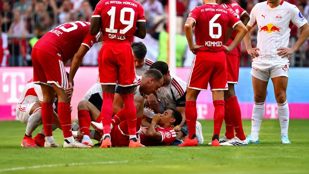 Bayern Munich players gather around Jamal Musiala after he collapses during the friendly match against RB Leipzig